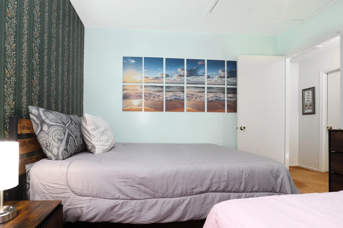 Bedroom featuring a bed with gray bedding, a beach-themed wall art piece, and a green patterned accent wall.