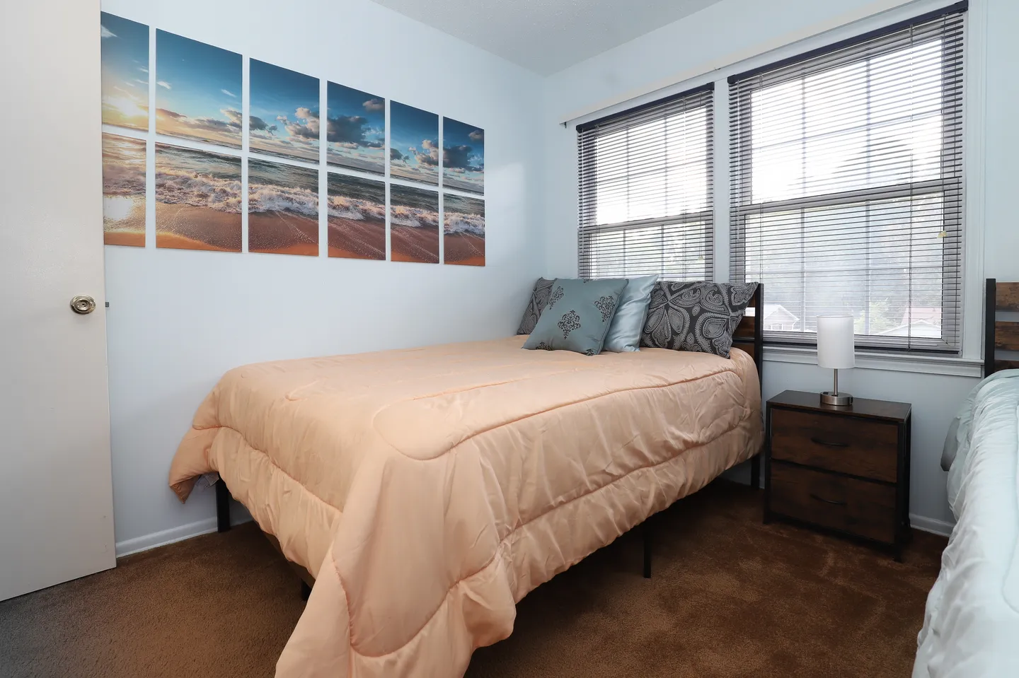 Bedroom featuring a bed with a peach comforter, a small nightstand with a lamp, and ocean-themed wall art.