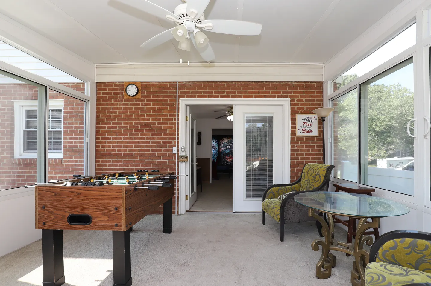 Sunroom with a foosball table, brick wall, large glass windows, and a glass-topped table with armchairs.