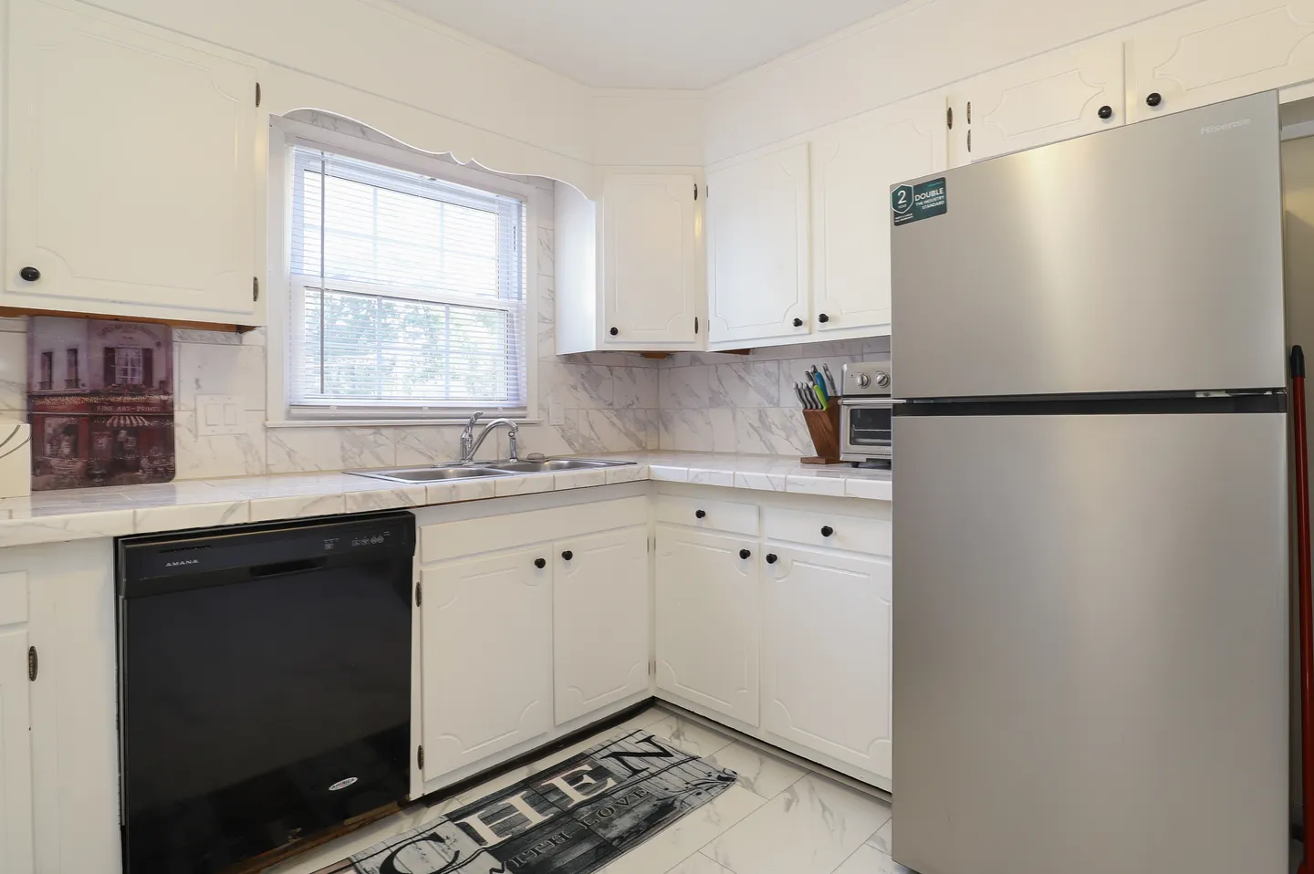 Kitchen corner with white cabinets, marble-patterned countertops, a black dishwasher, and a stainless steel refrigerator.