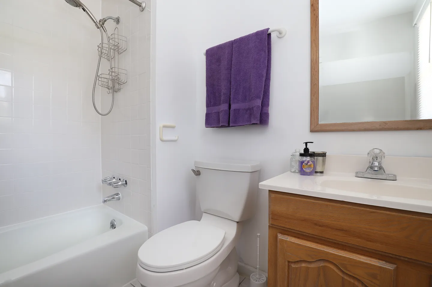 Bathroom with a bathtub shower combination, toilet, and wood vanity with framed mirror.