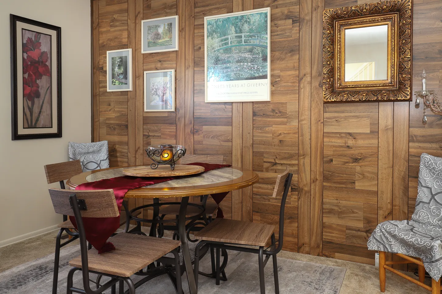 Dining area with a round table, metal-framed chairs, and an accent wall with wood-look paneling displaying framed art and a mirror.