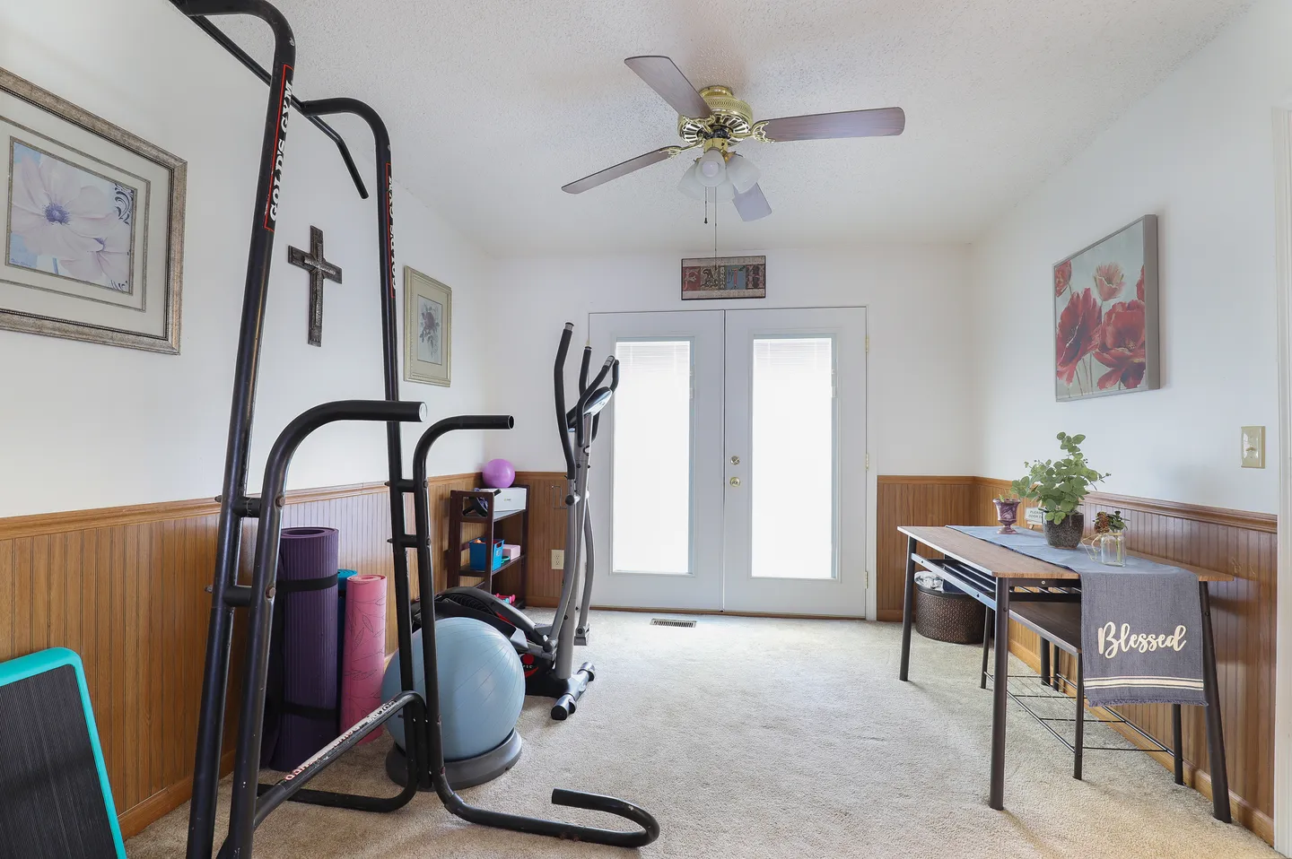 Indoor home gym and flex room with exercise equipment, carpeted floor, ceiling fan, and double doors.