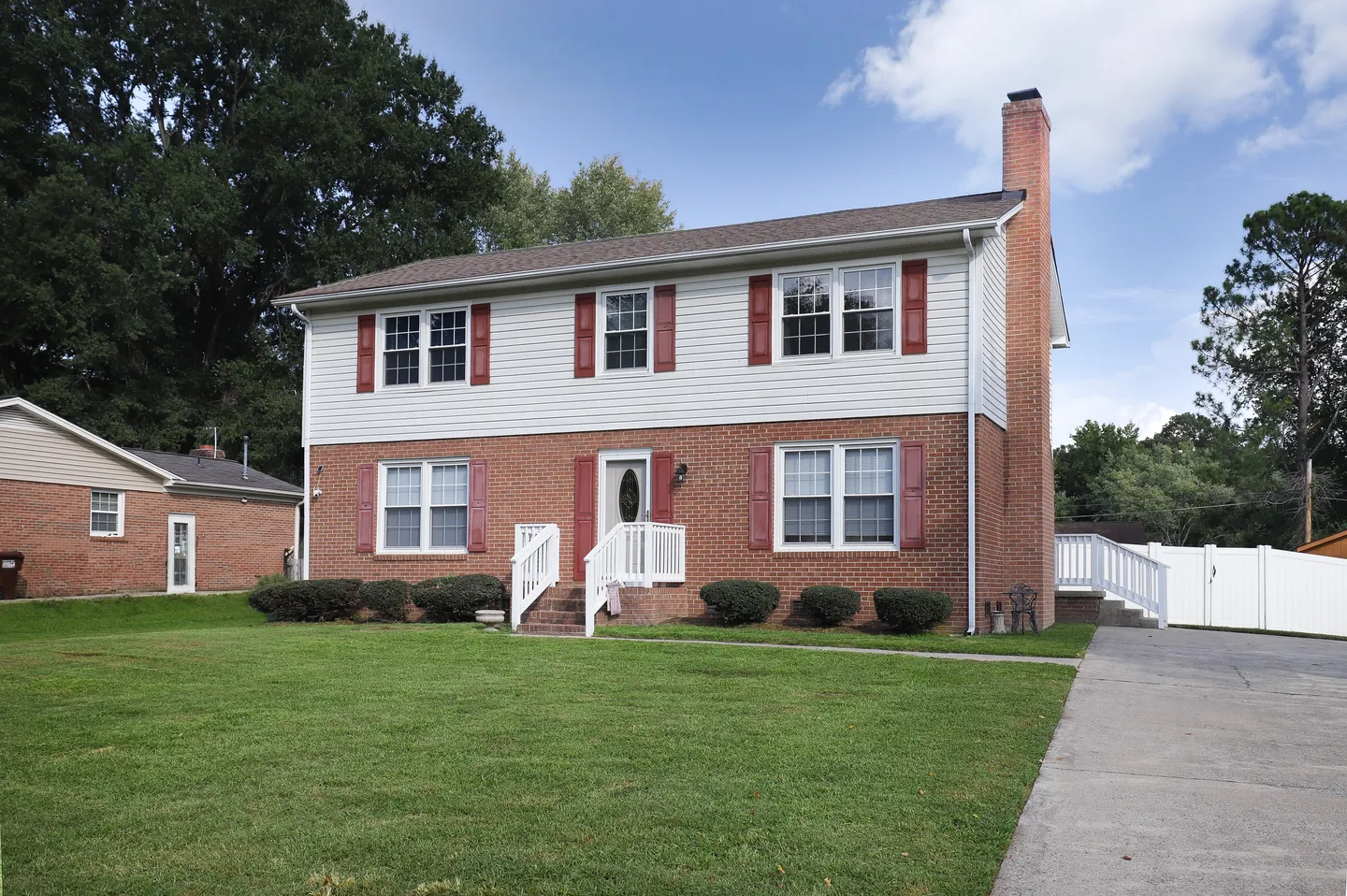 Exterior view of a two-story house with red brick on the lower level, white siding on top, red shutters, and a green front lawn.