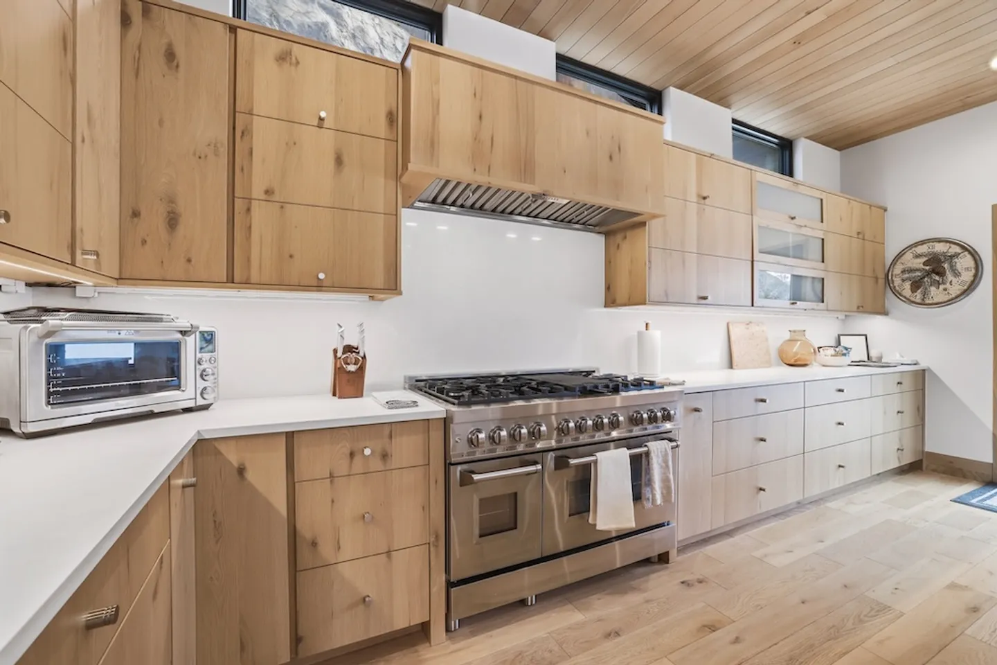 Kitchen counter with natural wood cabinets, white countertops, and a large stainless steel double-oven gas range.