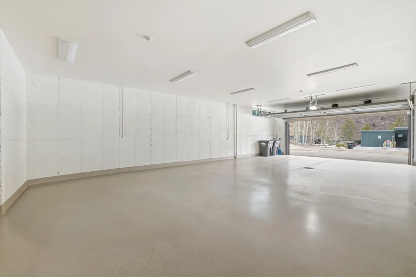 A spacious, empty multi-car garage with white walls and an open garage door looking out onto a paved driveway.