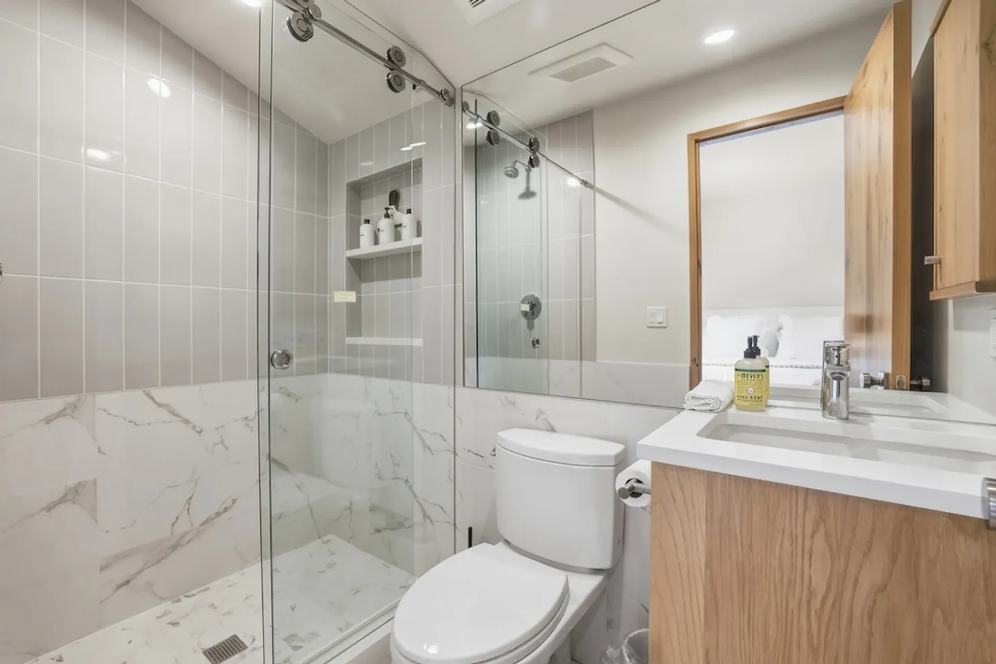 Modern bathroom featuring a glass-enclosed walk-in shower with tiled walls, a toilet, a light wood vanity, and a large mirror.