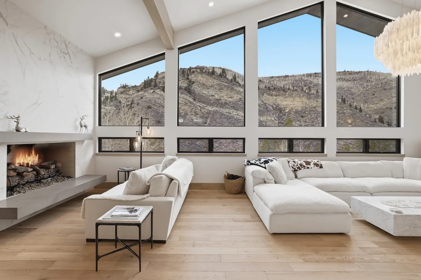 Bright living room with vaulted ceilings, large picture windows framing mountain views, a modern fireplace, and plush white sectional seating.