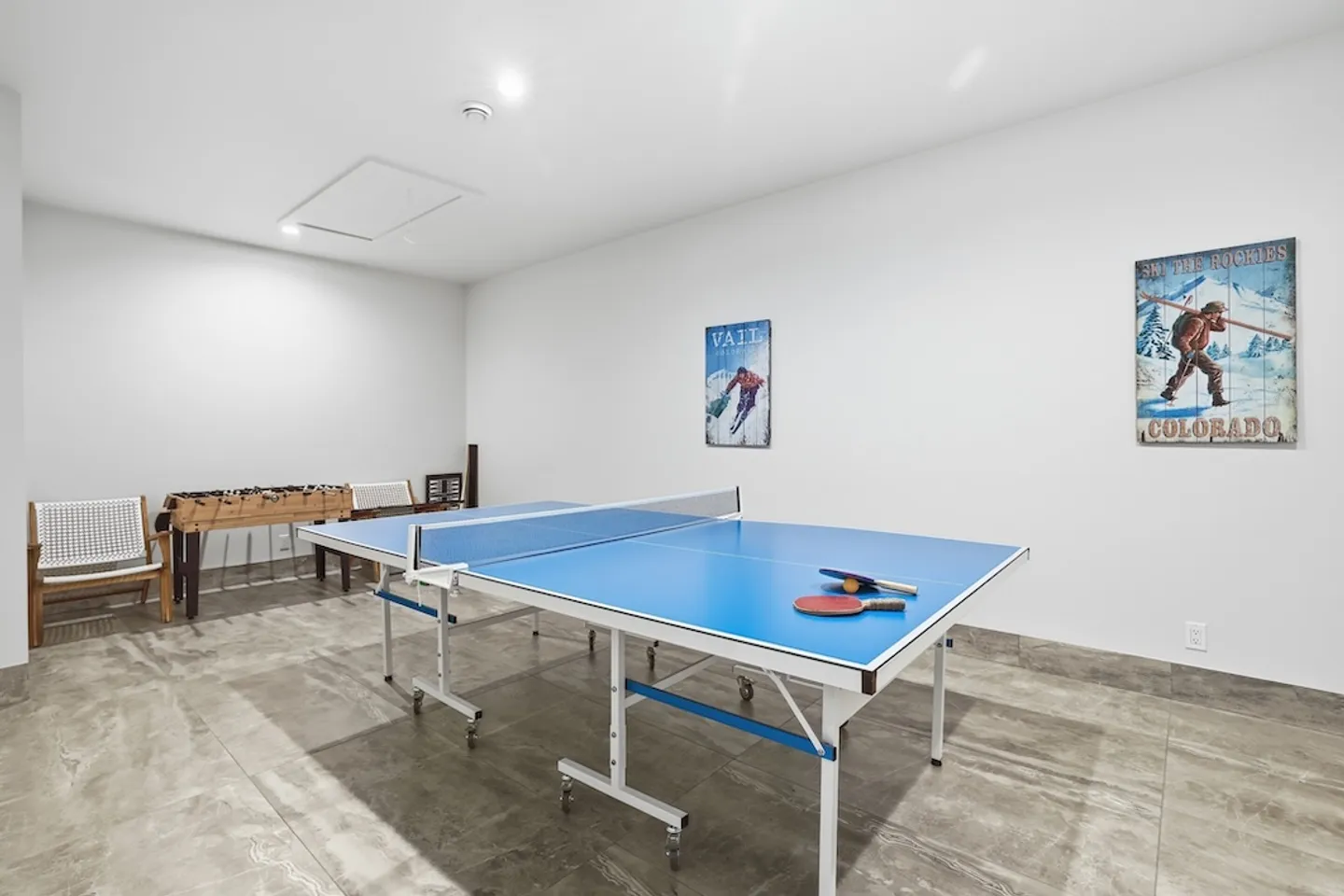 Game room featuring a blue ping pong table with paddles, a foosball table against the wall, tiled floors, and ski-themed wall art.
