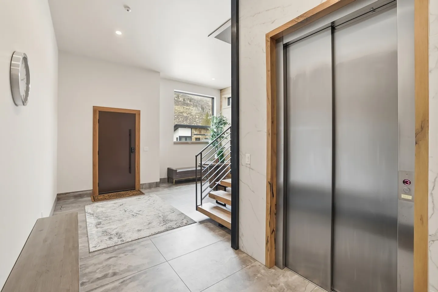 Modern entryway featuring an interior elevator with stainless steel doors, wooden stairs, and front door.