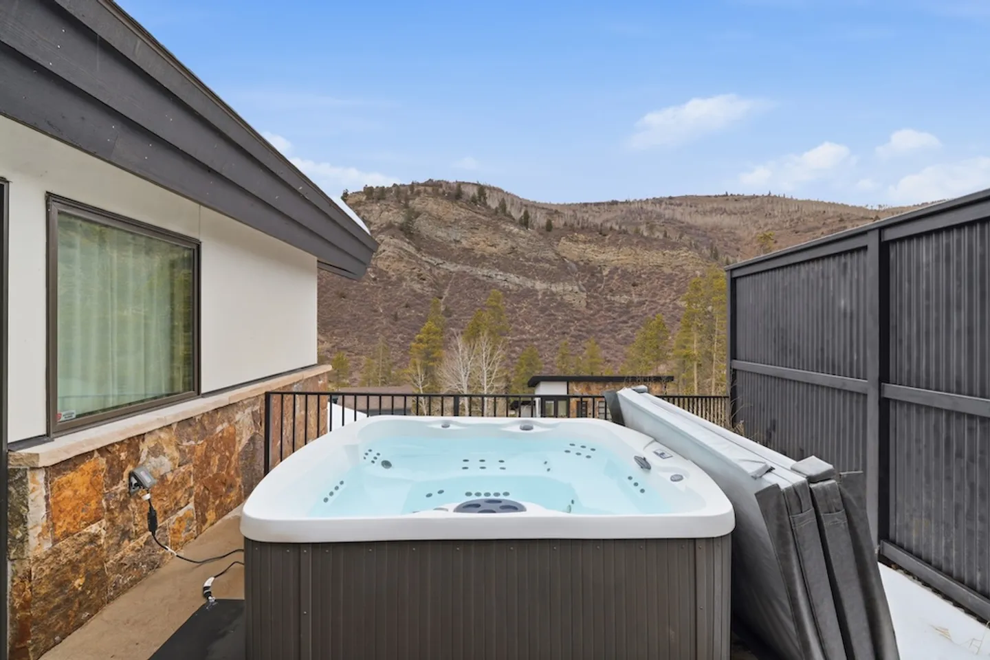 Outdoor hot tub on a balcony patio with views of nearby mountains and pine trees.