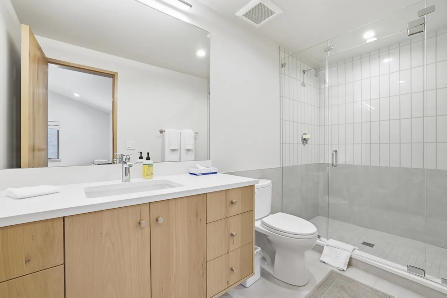 Bathroom with a light wood vanity, white countertop, large mirror, toilet, and glass-enclosed walk-in shower.