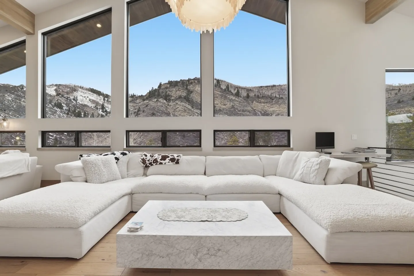 Living room featuring a large white U-shaped sectional sofa, low stone coffee table, and tall windows framing mountain views.