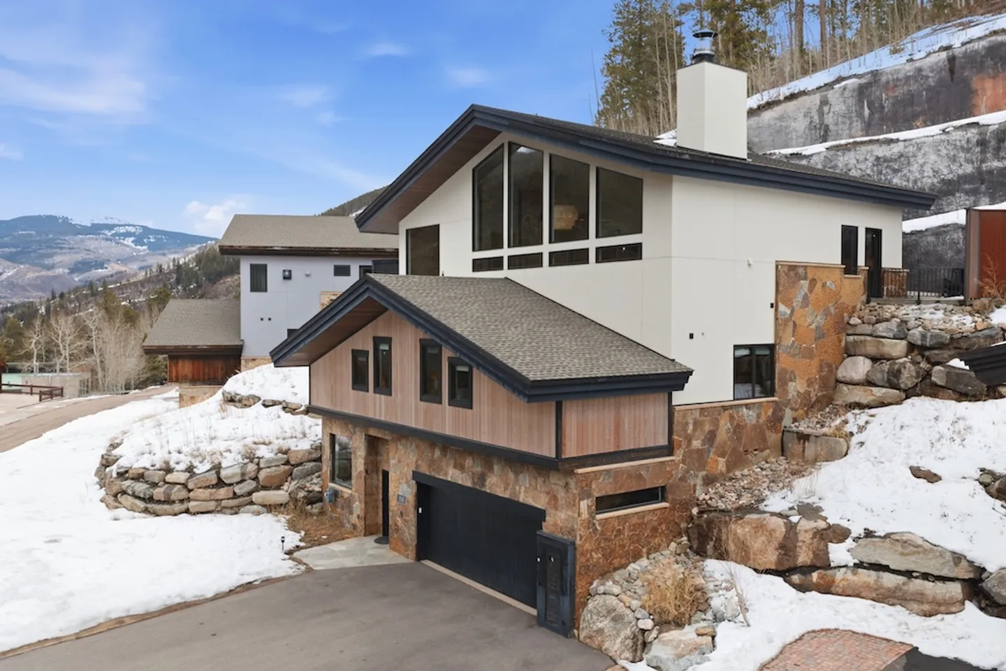 Exterior of a modern multi-level mountain home with stone, wood, and white siding built into a snowy hillside.