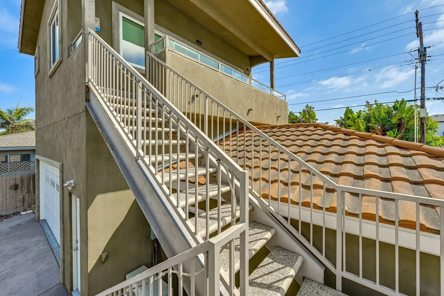 Exterior metal staircase leading to the upper deck of a multi-story home under a blue sky.