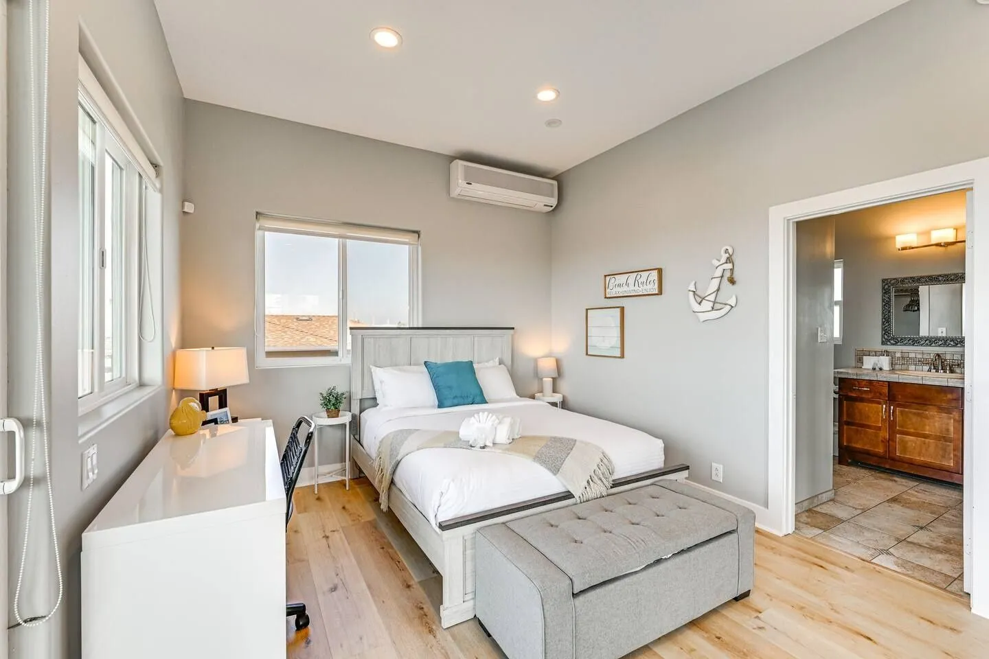 Bedroom with a wooden bed, white desk, upholstered storage bench, and an open doorway leading to an en-suite bathroom.
