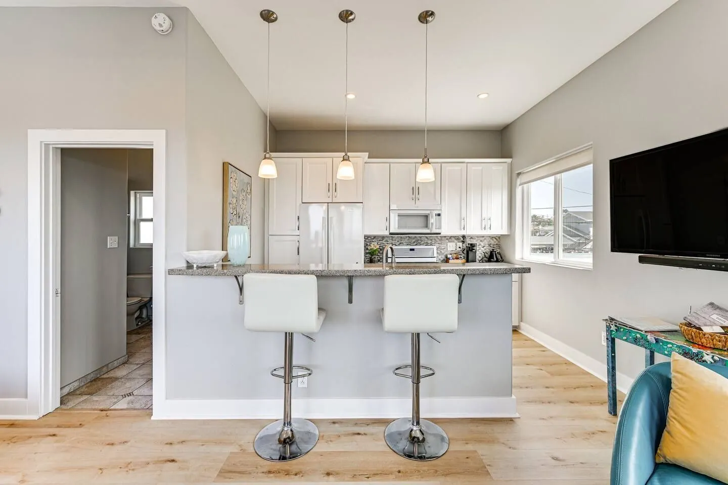 Kitchen with white cabinetry and a raised breakfast bar with two modern white barstools under three pendant lights.