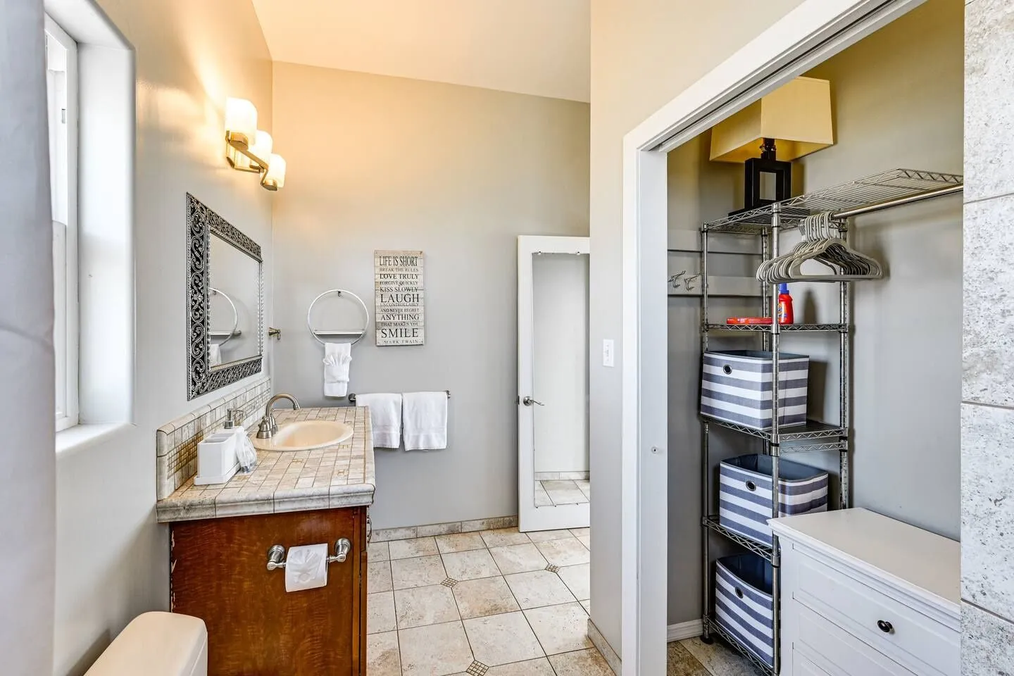 Bathroom with a tiled vanity, wooden cabinet, framed mirror, and an adjoining open closet with wire shelving.