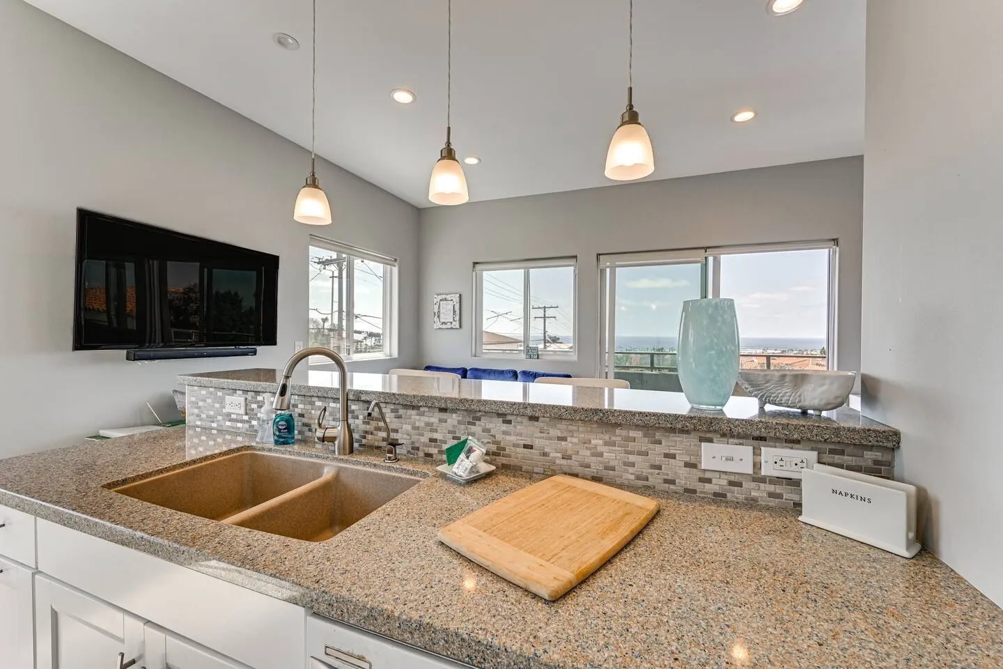 Kitchen counter and sink with view into living area and windows looking out to the ocean.