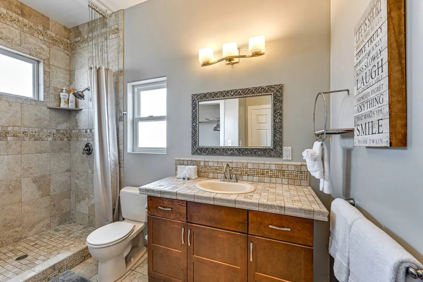 Bathroom with a wood vanity, tiled countertop, toilet, and walk-in tiled shower.