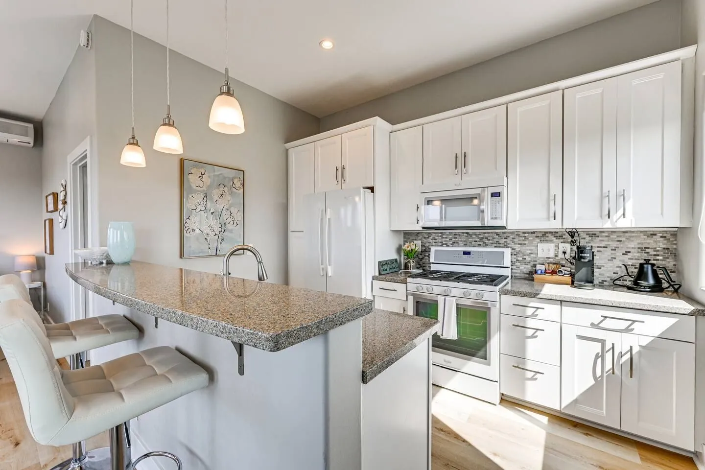 Bright kitchen featuring white cabinetry, speckled granite countertops, a breakfast bar with barstools, and white appliances.