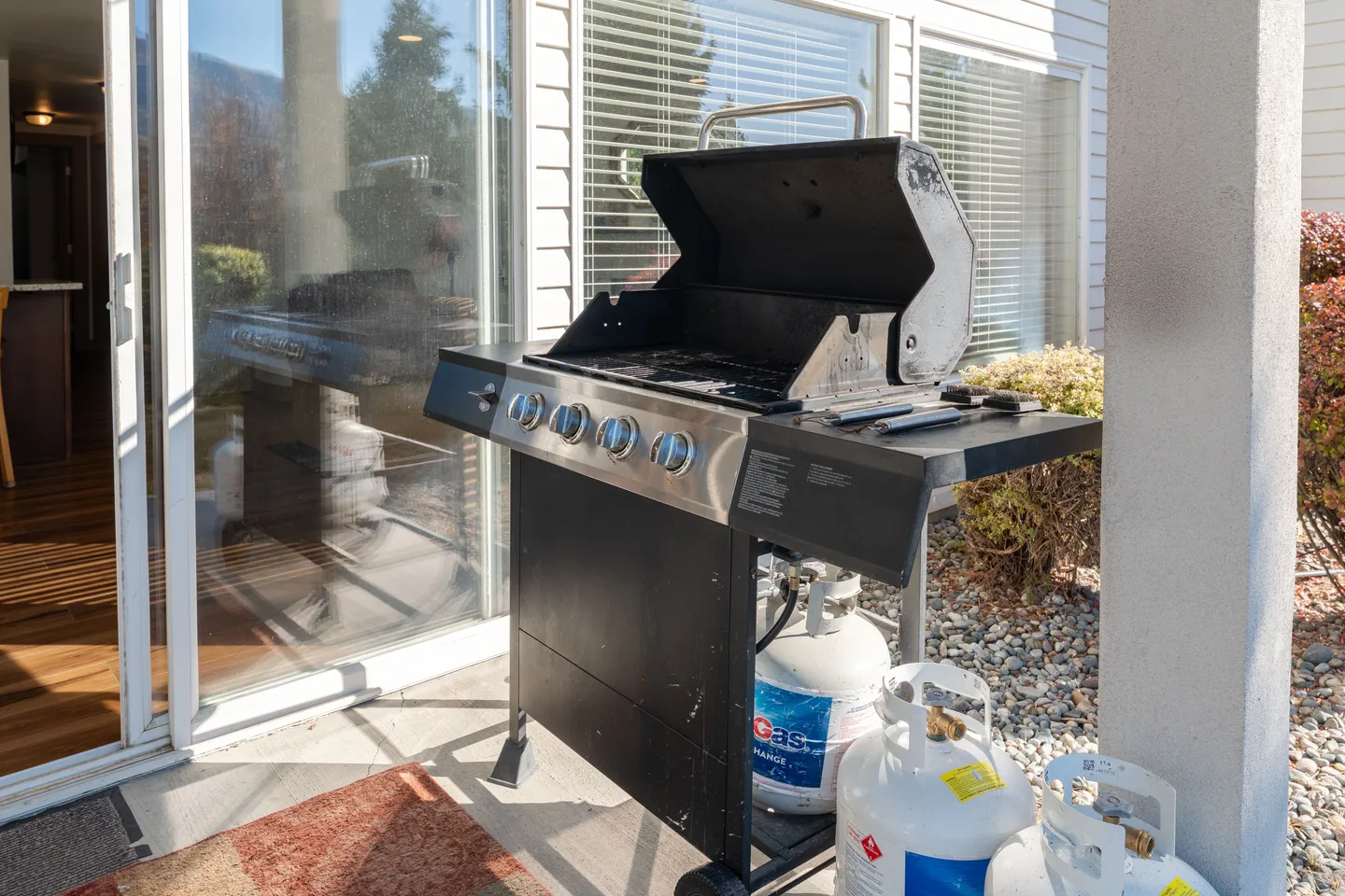 Open propane gas grill standing on a patio next to sliding glass doors.