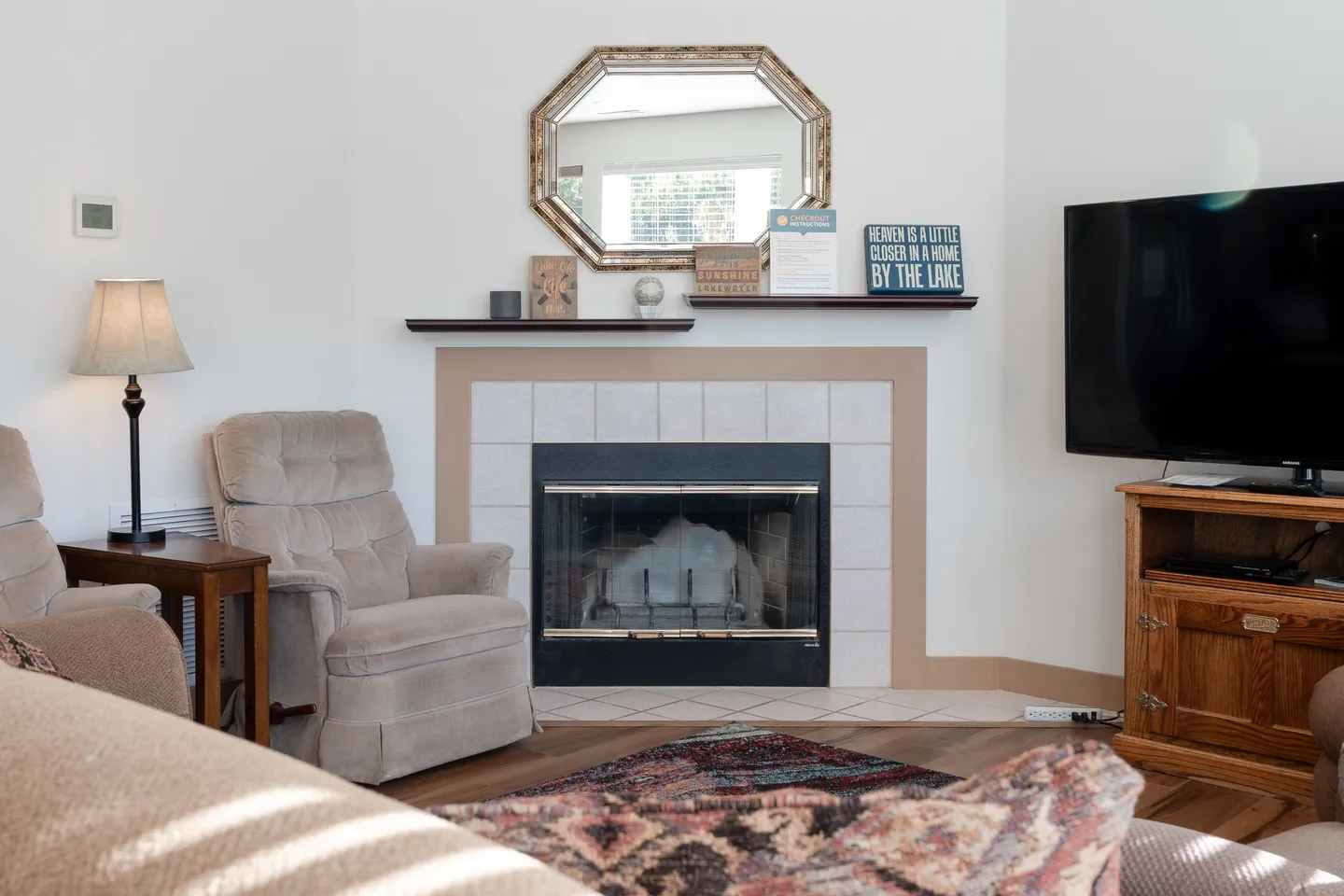 Living room corner featuring a tiled fireplace with a mantel, armchair, and a television on a wooden media stand.