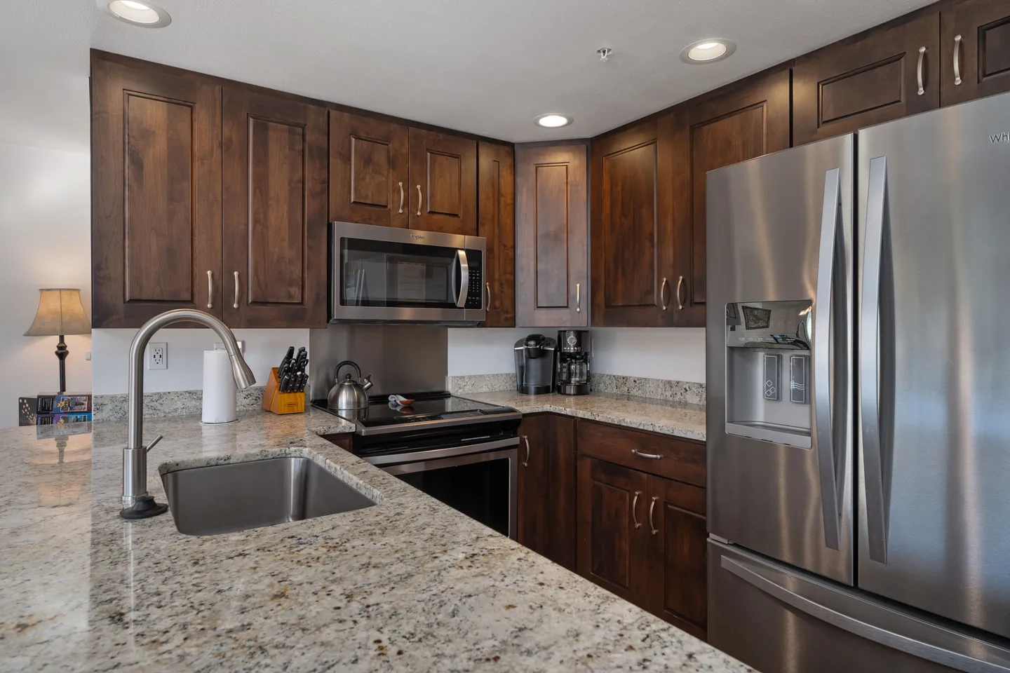 Kitchen featuring dark wood cabinetry, speckled granite countertops, an undermount sink, and stainless steel appliances.