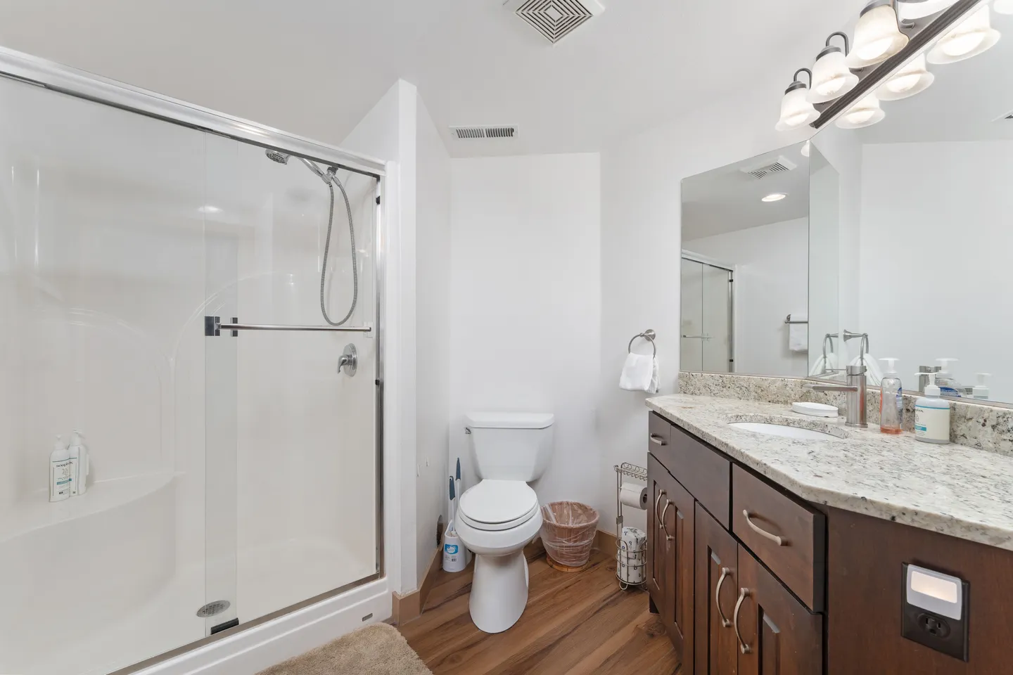 Bathroom with a glass-enclosed shower, dark wood vanity with granite countertop, and white toilet.