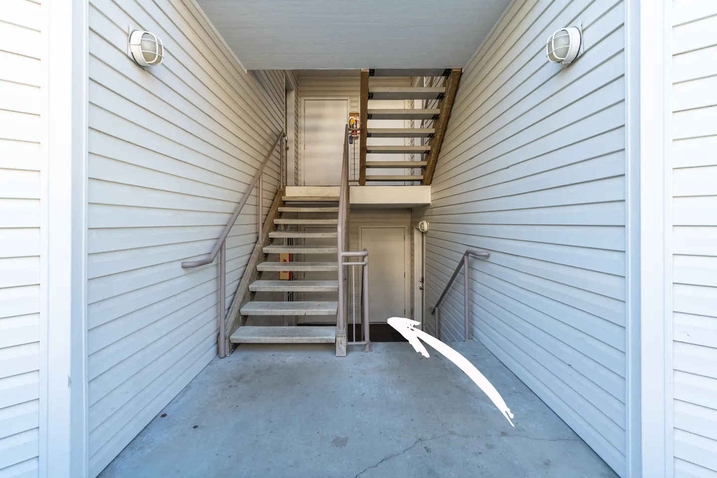Exterior covered breezeway with siding walls, concrete flooring, stairs leading up, and stairs leading down to a lower entrance.