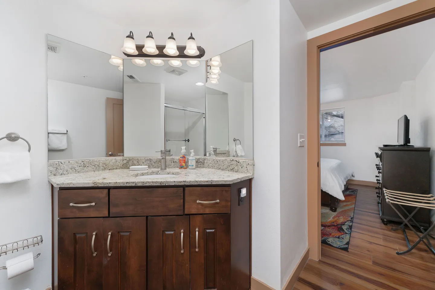 Bathroom vanity with speckled countertop and dark wood cabinets next to an open doorway leading to a bedroom.