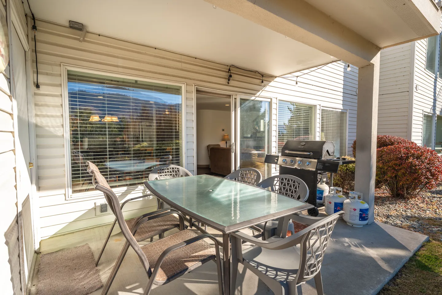 Covered patio featuring an outdoor dining table with chairs and a barbecue grill next to large windows and a sliding glass door.