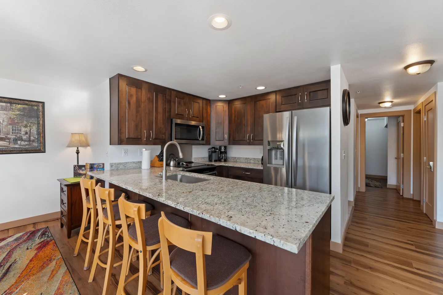 Kitchen with dark wood cabinets, speckled granite countertops, a stainless steel refrigerator, and breakfast bar seating.