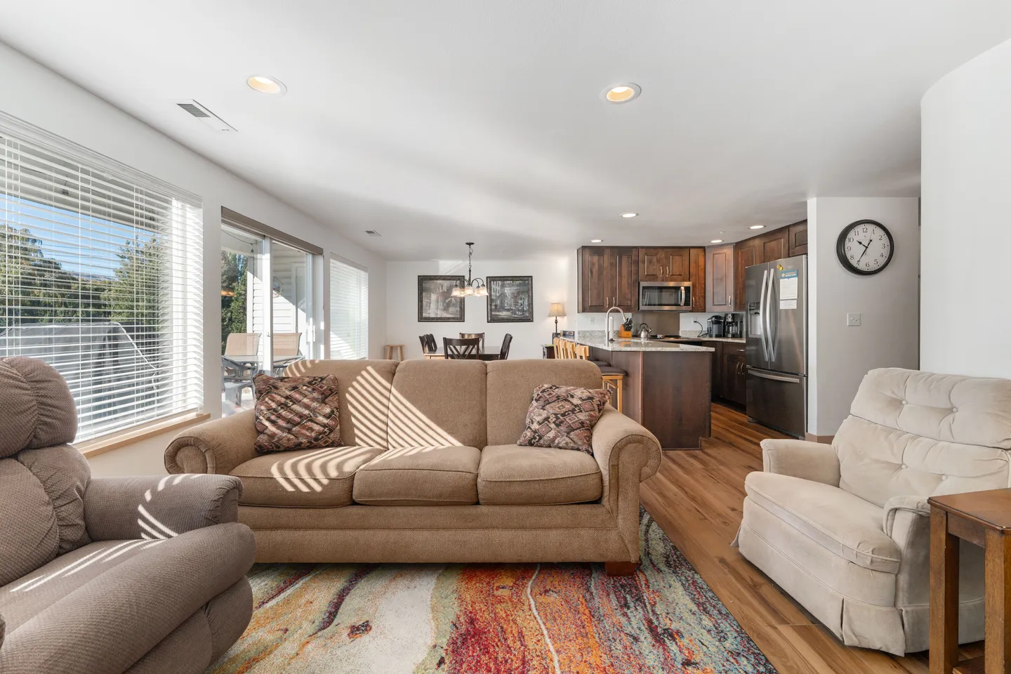 Open-concept living room with a brown sofa, recliner chairs, and a colorful rug, looking toward the kitchen and dining area.