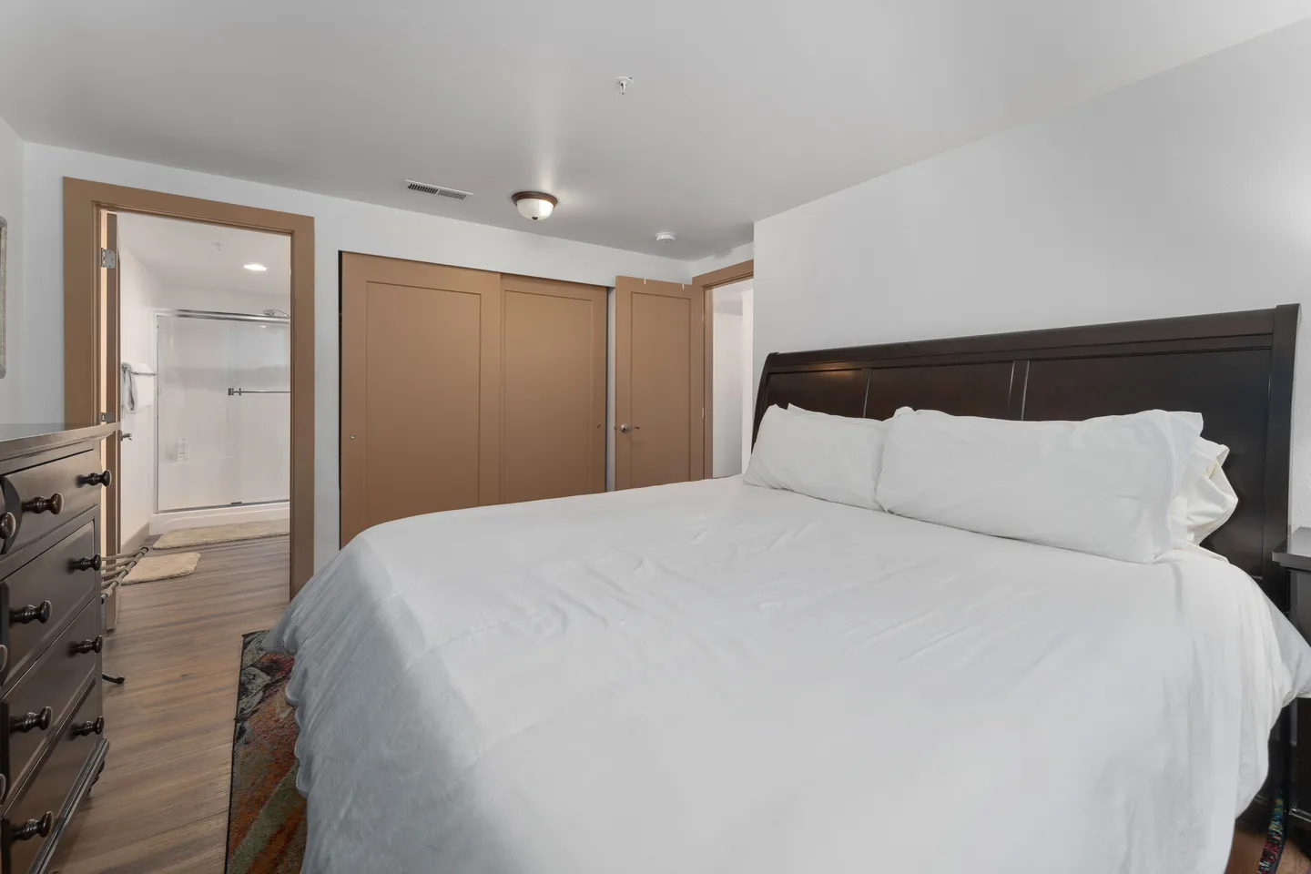 Bedroom with a large bed, dark wood headboard, dresser, sliding closet doors, and an open doorway leading to an en-suite bathroom.