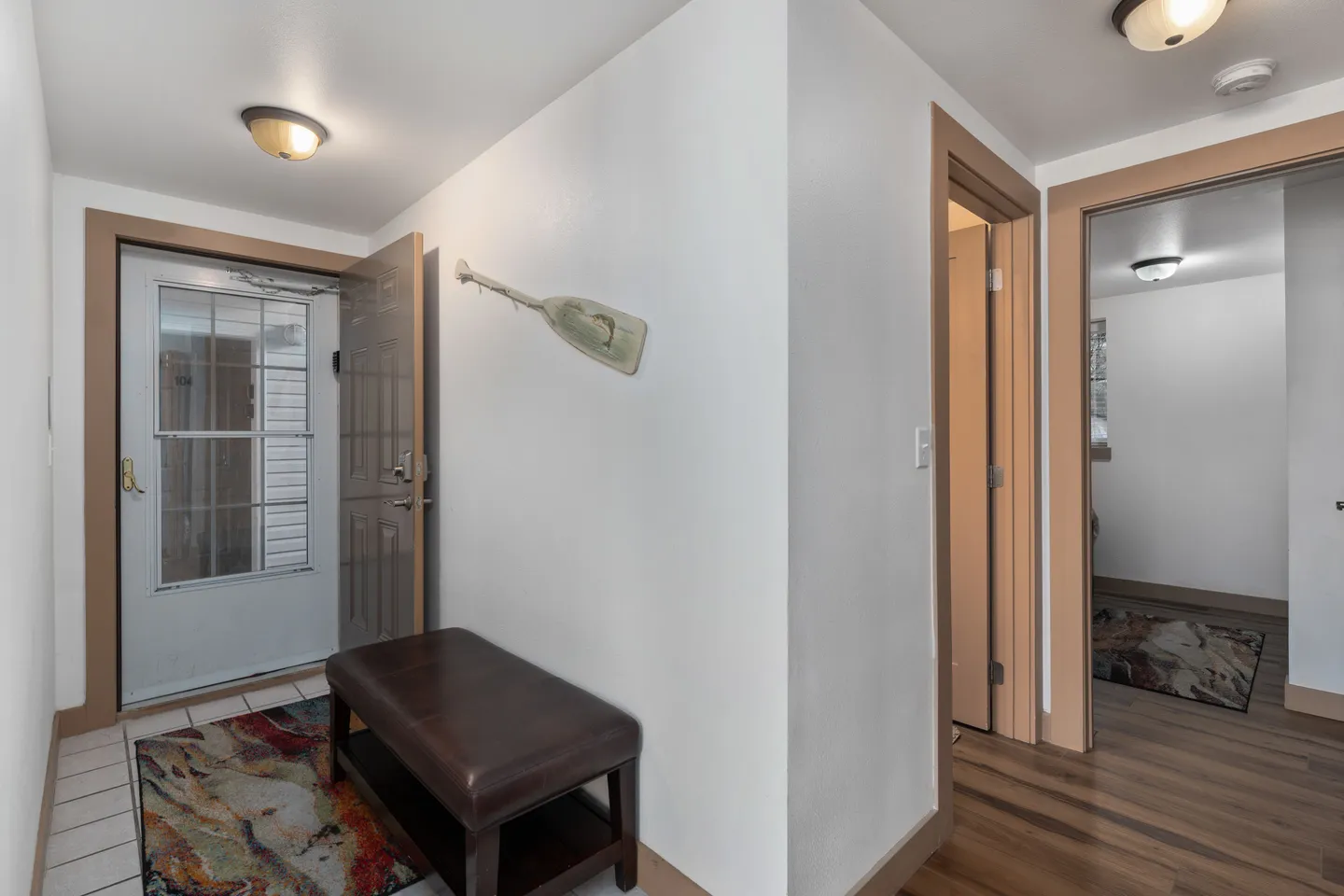 Front entry hall with an open door, brown bench, tiled entry area, and a decorative paddle on the wall.