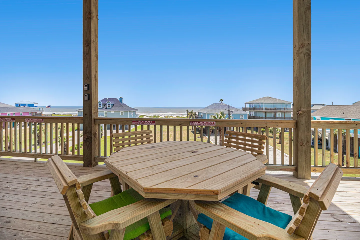 A wooden octagon-shaped outdoor dining table and chairs on an elevated deck overlooking the ocean in the distance.