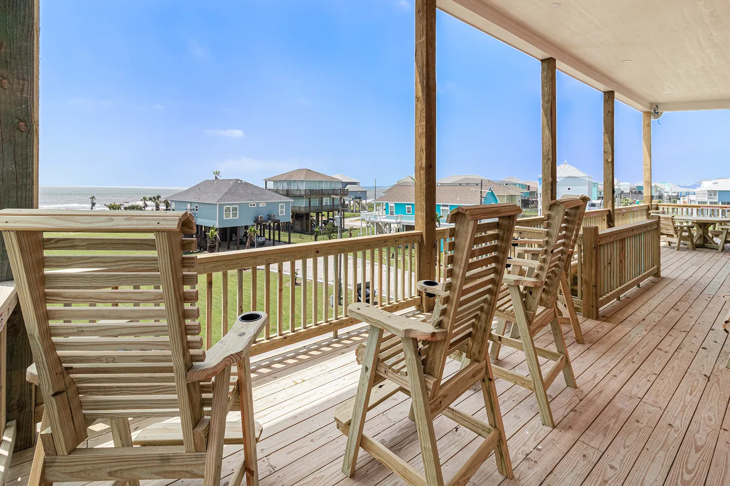Elevated covered wooden deck with wooden chairs overlooking neighboring coastal homes and the ocean.