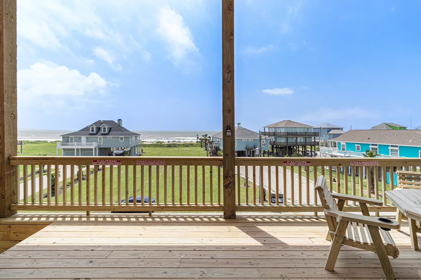 Elevated wooden deck with railing and outdoor seating overlooking neighboring coastal houses and the ocean.