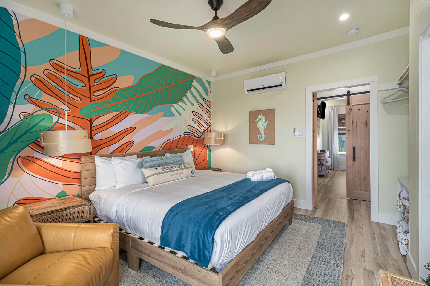Bedroom with a tropical plant mural behind a wooden platform bed and an armchair in the foreground.