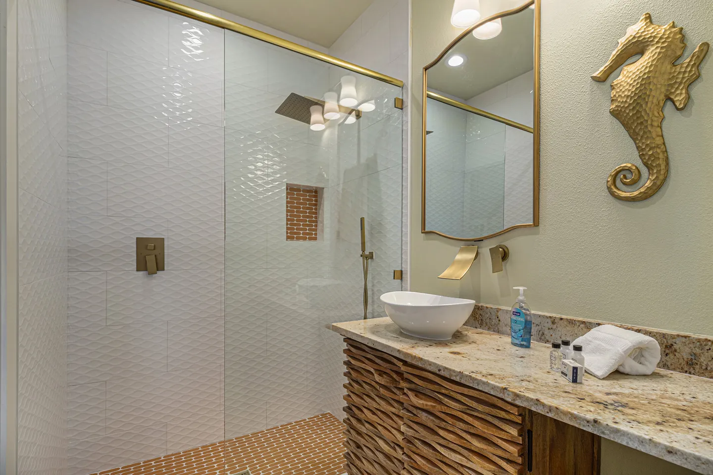 Bathroom with a textured wood vanity, vessel sink, gold-framed mirror, and a glass-enclosed walk-in shower with textured tile.