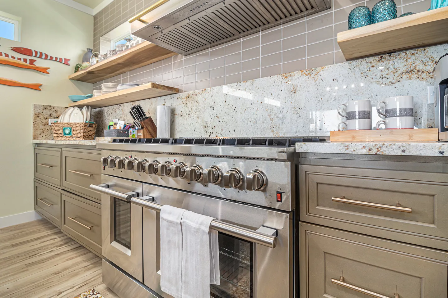 Kitchen counter area featuring a large stainless steel double oven range, granite countertops, tile backsplash, and open shelving.