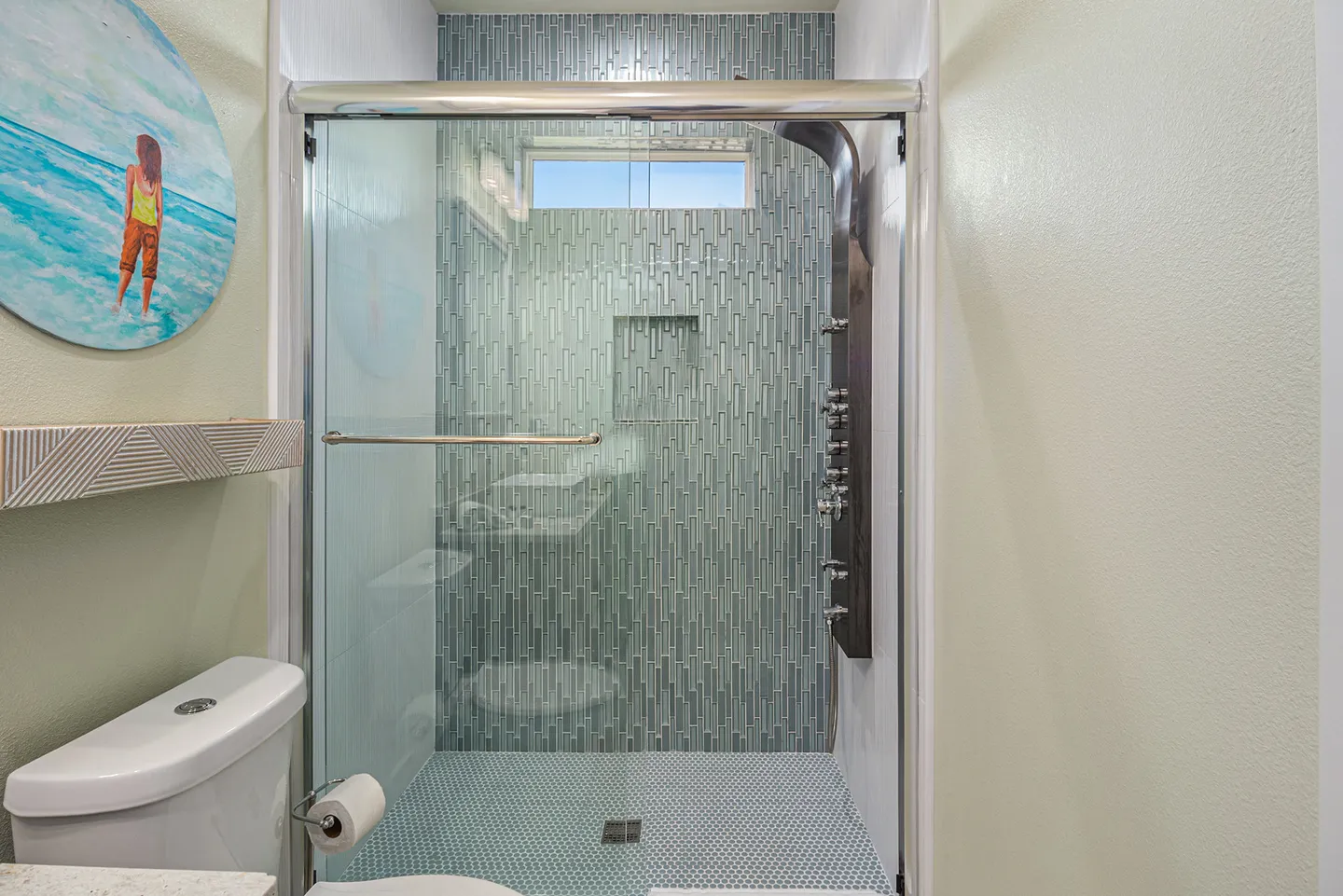 Bathroom showing a walk-in shower with sliding glass doors, blue tile, and a multi-jet shower panel next to a toilet.