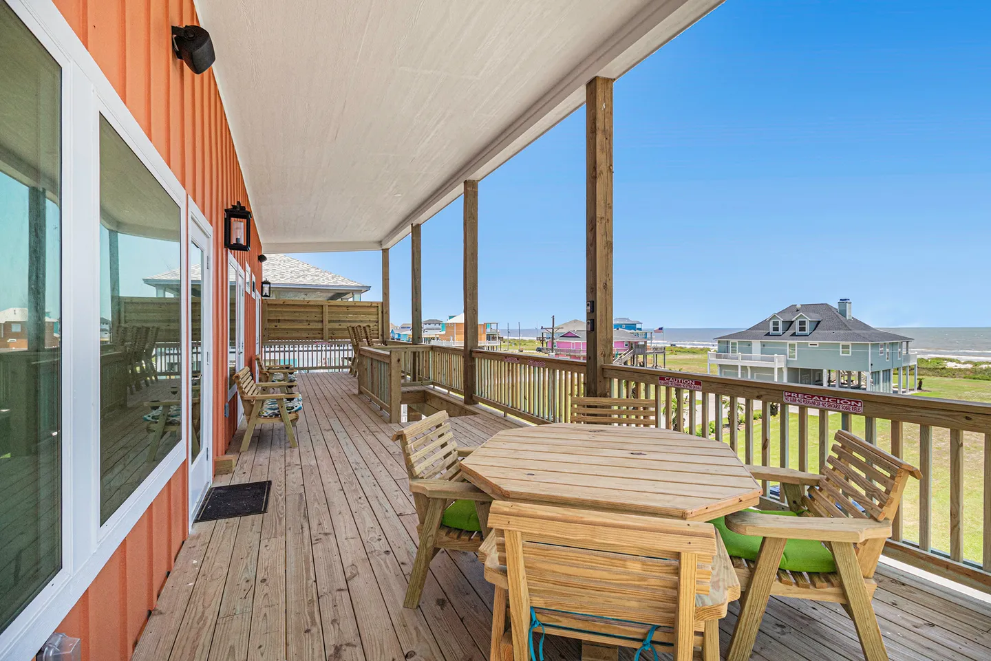 Covered wooden deck with outdoor dining table, chairs, and a view of neighboring houses and the sea.