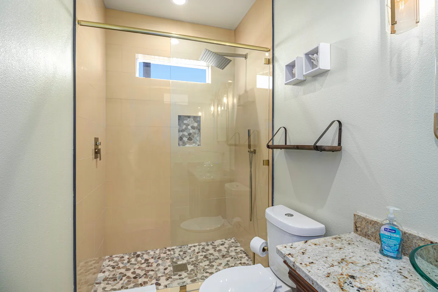 Bathroom showing a glass-enclosed walk-in shower with pebble-tile floor next to a toilet and vanity counter.