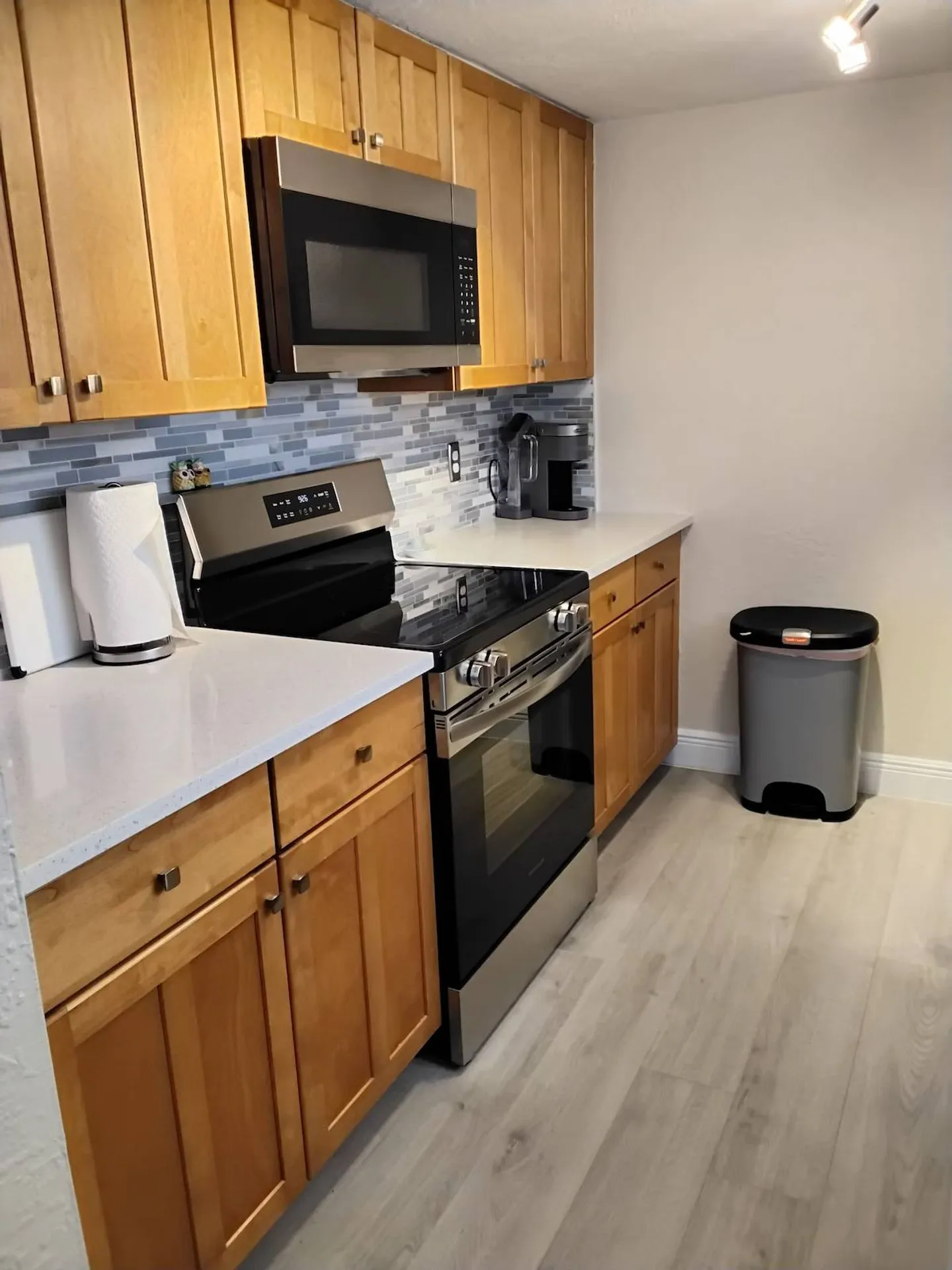Kitchen counter featuring wood cabinetry, stainless steel oven and microwave, white quartz countertop, and light plank flooring.