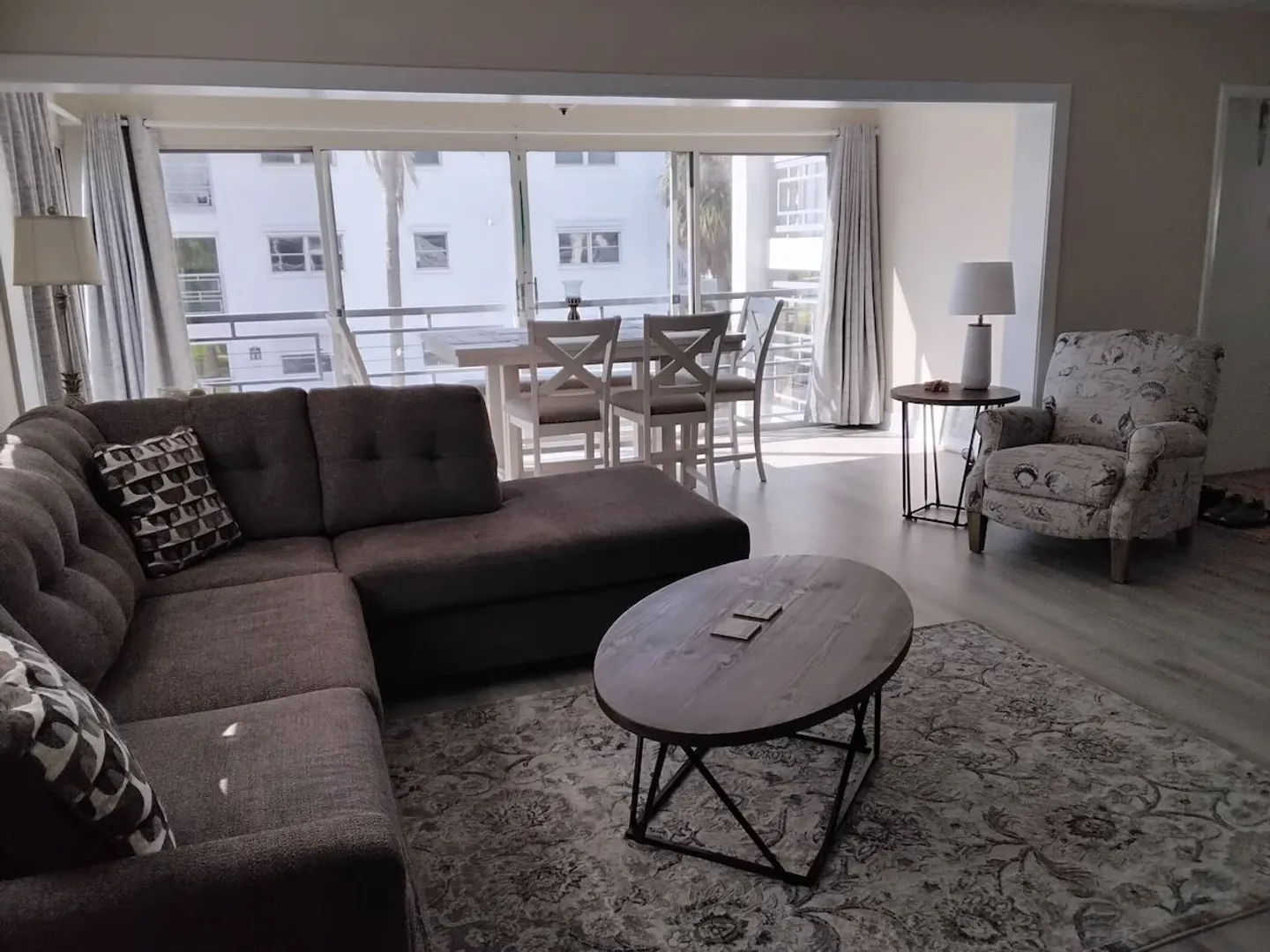 Living room with an L-shaped sectional sofa, oval coffee table, armchair, and an adjacent dining area near large sliding glass doors.
