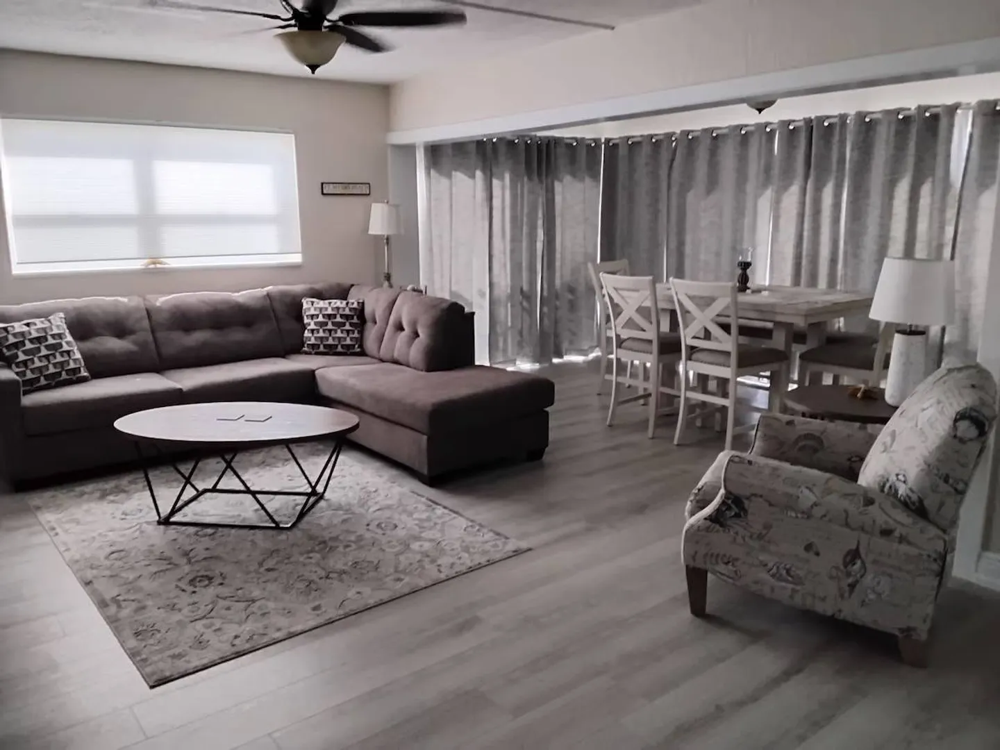 Living and dining area featuring a sectional sofa, coffee table, patterned armchair, and adjacent dining table with chairs.