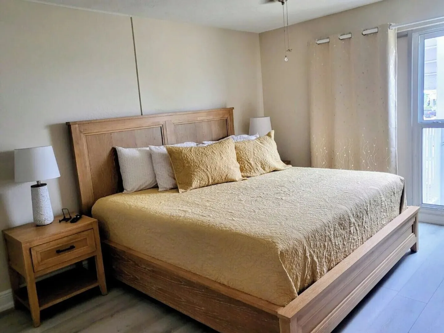 Bedroom with a wooden bed, yellow bedding, matching nightstand, and sliding glass door with curtains.