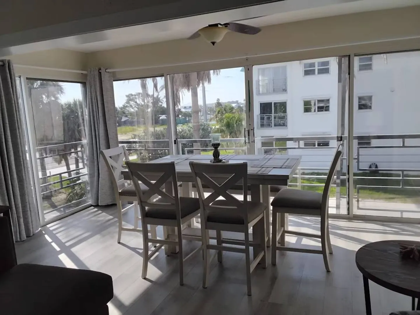 Dining area with a wooden table and cushioned chairs surrounded by large sliding glass doors.